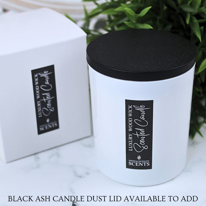 White candle with black lid and 'Luxury Wood Wick' branding on a marble surface with greenery in the background.