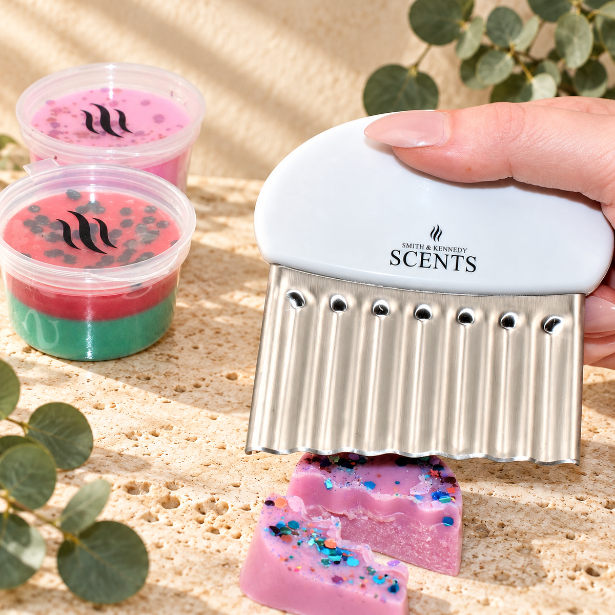 Smith & Kennedy Scents wax melt cutter with white branded handle and silver crinkle blade, held above cut pink wax.